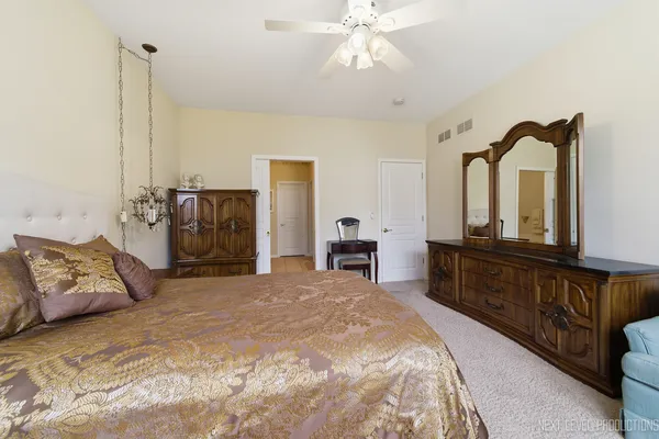 a spacious bedroom with a bed a dresser and potted plants with wooden floor