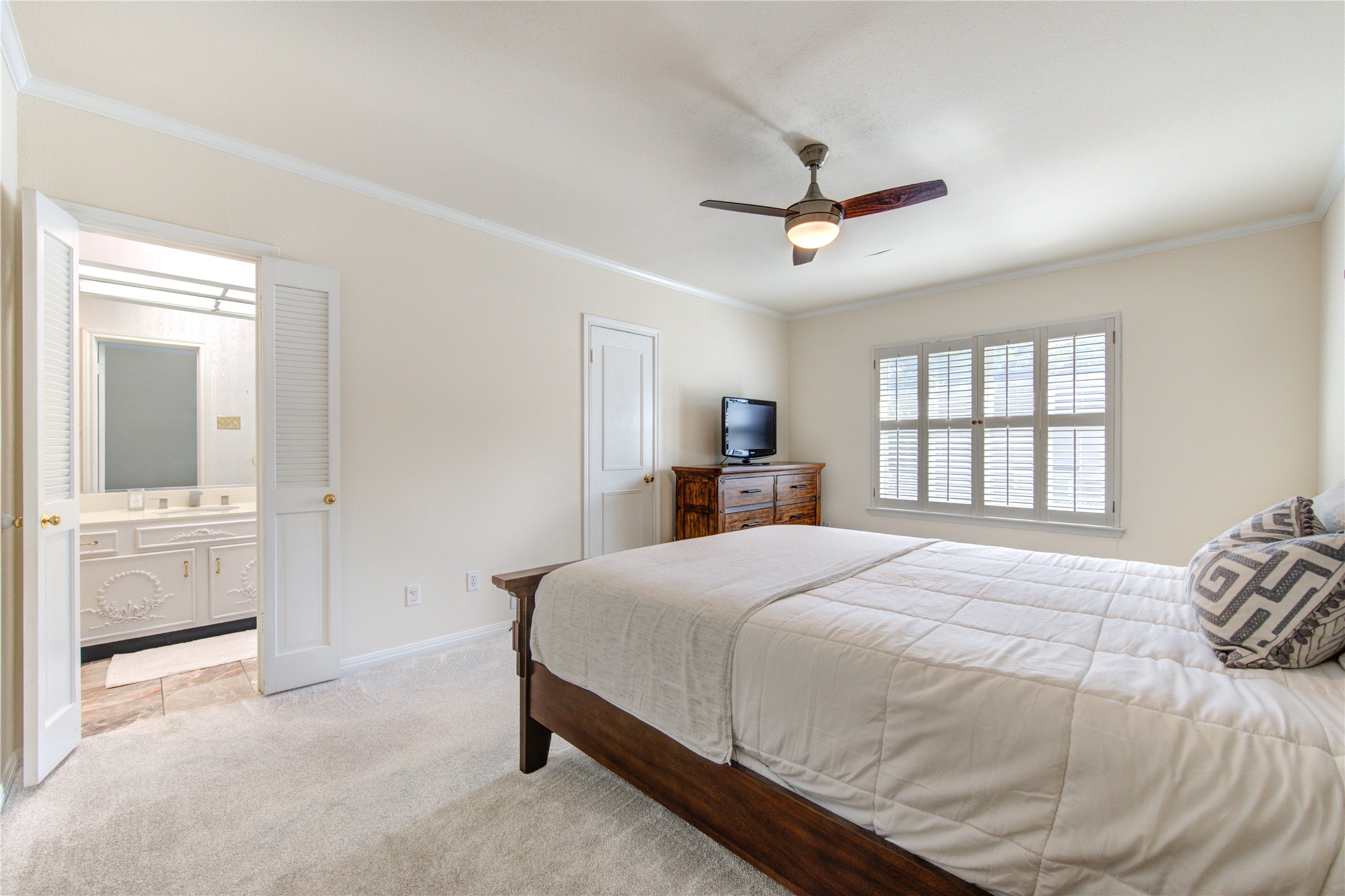 2232 South Piney Point Road, Unit 110 Houston, TX 77063 - Photo 11 of 21 Spacious primary suite filled with natural light, featuring plush carpeting, elegant plantation shutters, ceiling fan, and direct access to a private ensuite bath for added comfort and privacy.