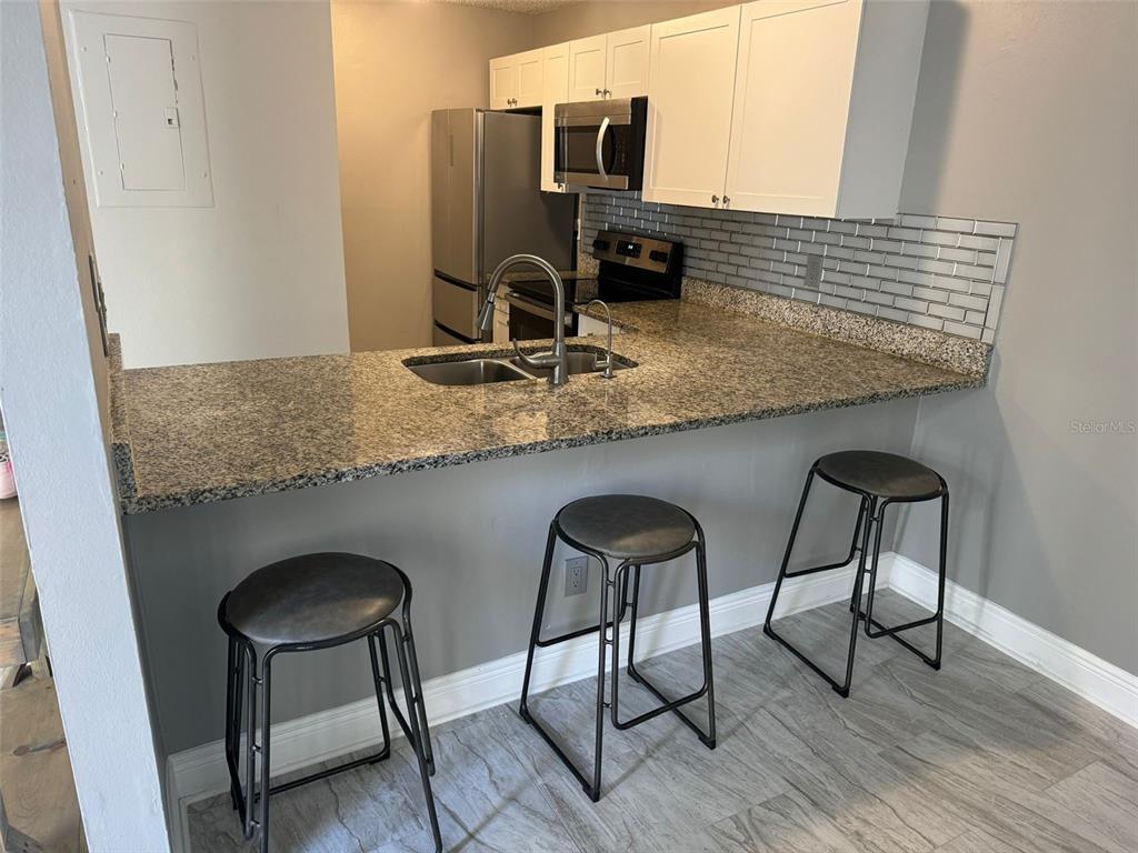 1030 Abada Court Northeast, Unit 110 Palm Bay, FL 32905 - Photo 4 of 10 a kitchen with granite countertop a counter space chairs and microwave