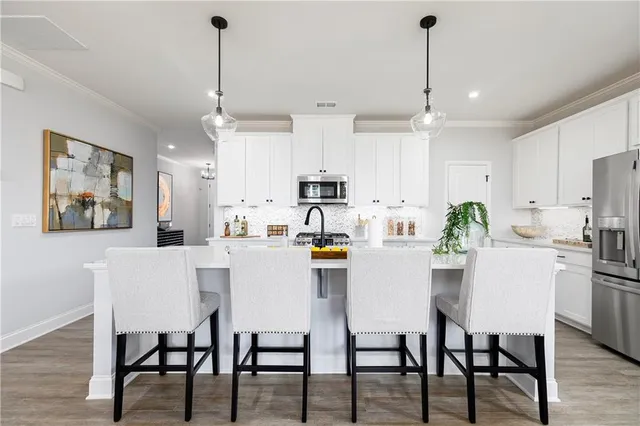 a kitchen with stainless steel appliances a white refrigerator a stove a sink a dining table and chairs with wooden floor