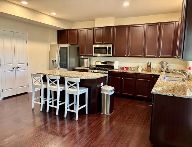 a kitchen with stainless steel appliances granite countertop wooden floors a stove top oven a sink with island and chairs