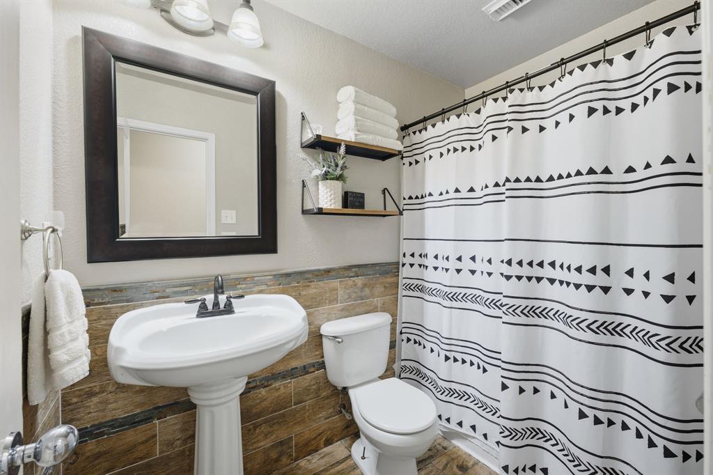 14152 Rodeo Daze Drive Fort Worth, TX 76052 - Photo 18 of 20 Pedestal sink with dark-toned faucet, framed mirror, and warm-toned tile wainscoting