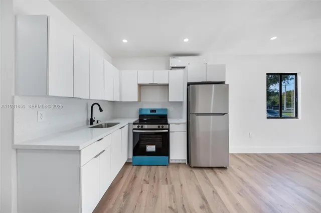 a kitchen with stainless steel appliances granite countertop a refrigerator stove a sink and white cabinets with wooden floor