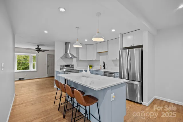 a kitchen with stainless steel appliances granite countertop a refrigerator a sink dishwasher a stove and white countertops with wooden floor