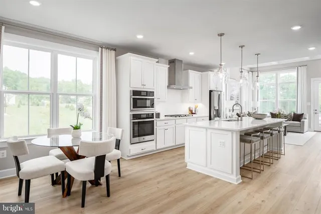 a kitchen with stainless steel appliances granite countertop a table chairs sink and white cabinets