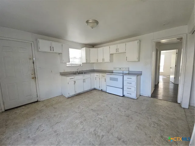a large white kitchen with a sink and refrigerator