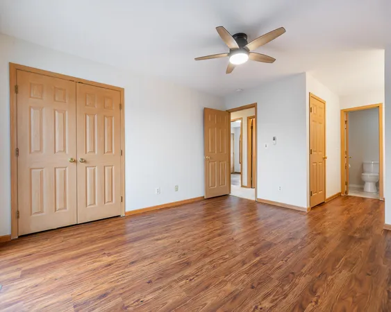 an empty room with wooden floor ceiling fan and windows