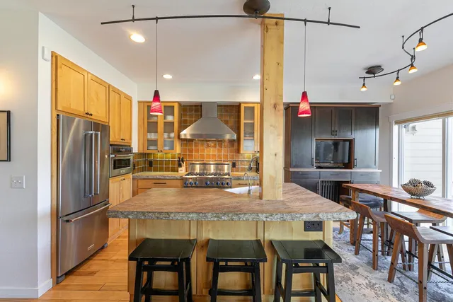 a kitchen with stainless steel appliances a dining table chairs refrigerator and sink