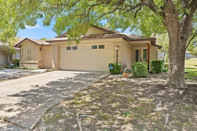 a view of a white house next to a yard with a large tree