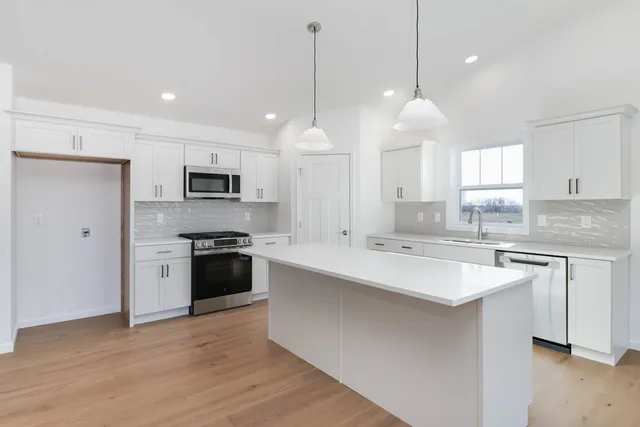 a large kitchen with white cabinets a sink a window and stainless steel appliances