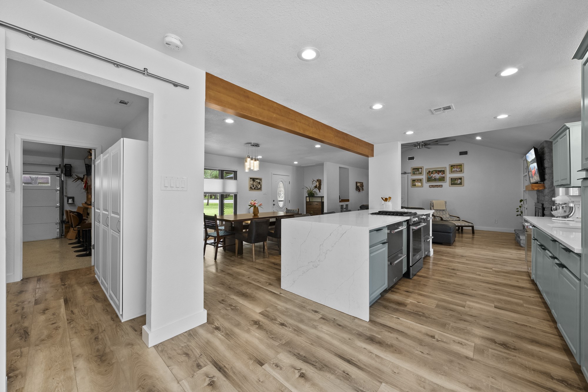 2802 Robin Road Manchaca, TX 78652 - Photo 8 of 40 Open-concept kitchen featuring light wood-finish flooring, a waterfall island with a built-in range, recessed lighting, light-toned cabinetry, and a wood beam accent