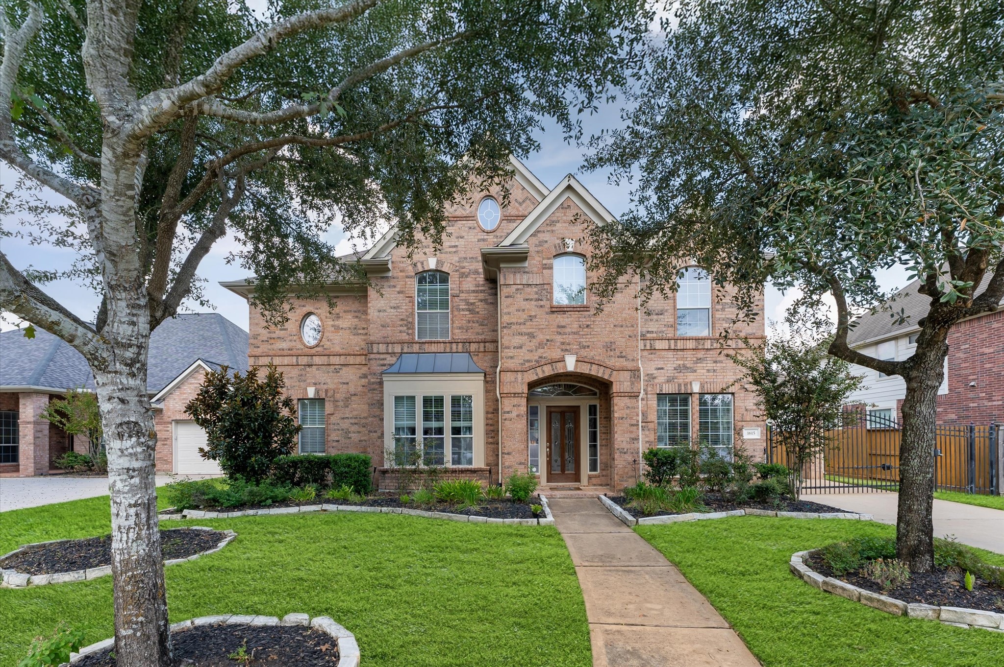 1615 Noble Pointe Drive Spring, TX 77379 - Photo 1 of 50 This photo showcases a charming two-story brick home with a symmetrical facade and large windows. The front yard features well-maintained landscaping with mature trees and a curved pathway leading to the entrance.