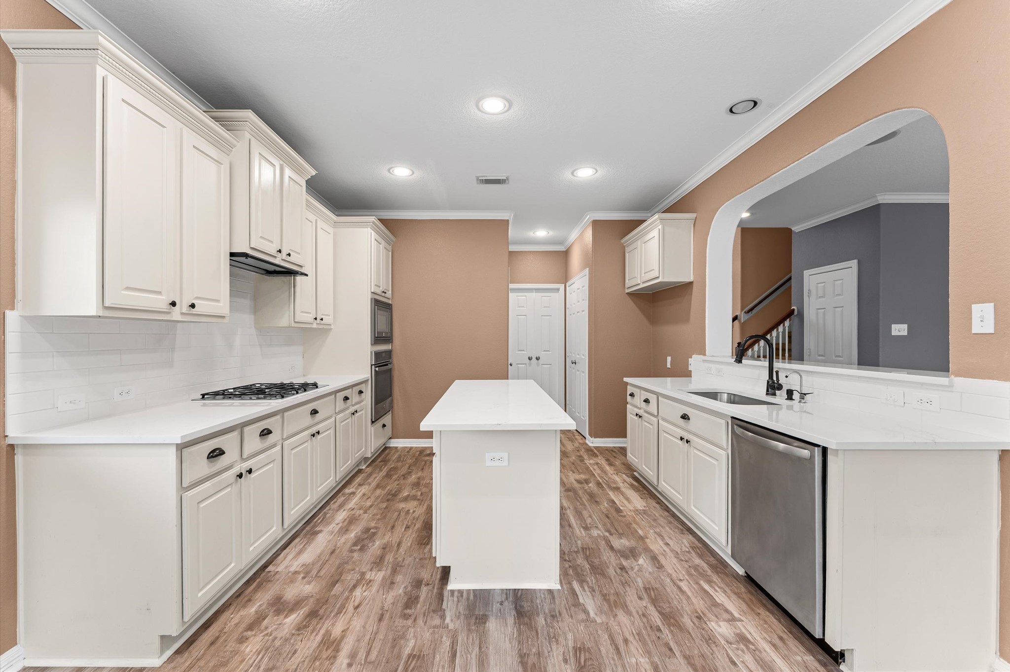 1615 Noble Pointe Drive Spring, TX 77379 - Photo 14 of 50 This kitchen features a spacious layout with white cabinetry, quartz countertops, and stainless steel appliances. The wood-style flooring and neutral tones create a warm and inviting atmosphere. An island provides additional workspace, and there's ample storage for convenience.