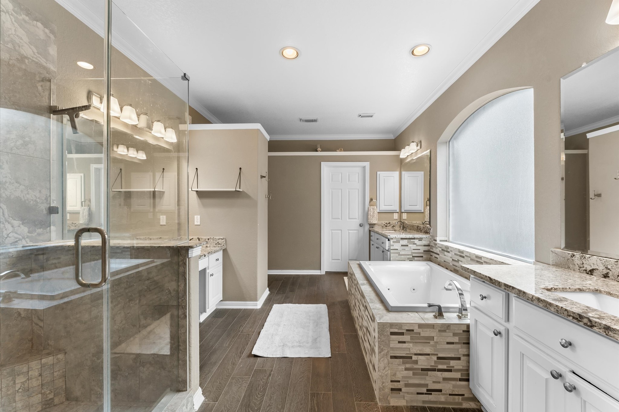 1615 Noble Pointe Drive Spring, TX 77379 - Photo 23 of 50 This spacious bathroom features elegant granite countertops, a large glass-enclosed shower, and a luxurious soaking tub. The room is well-lit with recessed lighting and a large frosted window, offering both privacy and natural light. The dark wood flooring adds warmth and contrast to the neutral-toned walls and white cabinetry.