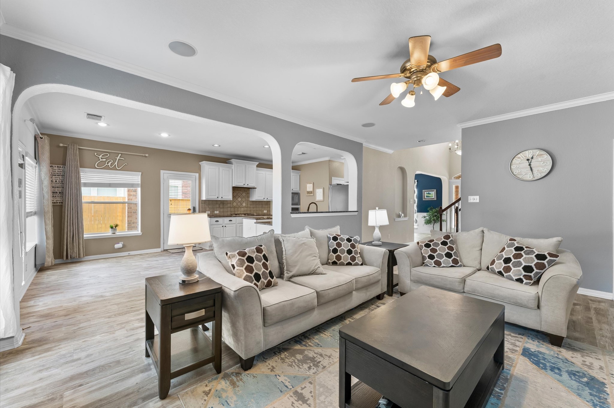 1615 Noble Pointe Drive Spring, TX 77379 - Photo 10 of 50 This photo showcases a spacious, open-concept living area with neutral tones and stylish decor. It features comfortable seating, a ceiling fan, and ample natural light. The room flows seamlessly into a modern kitchen with white cabinetry and a cozy dining nook. Ideal for entertaining and family living.