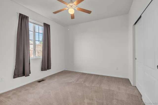 an empty room with chandelier fan and windows