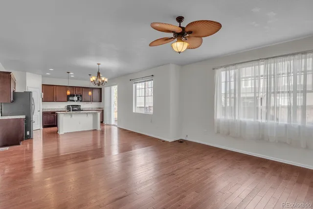 an empty room with wooden floor a ceiling fan and windows