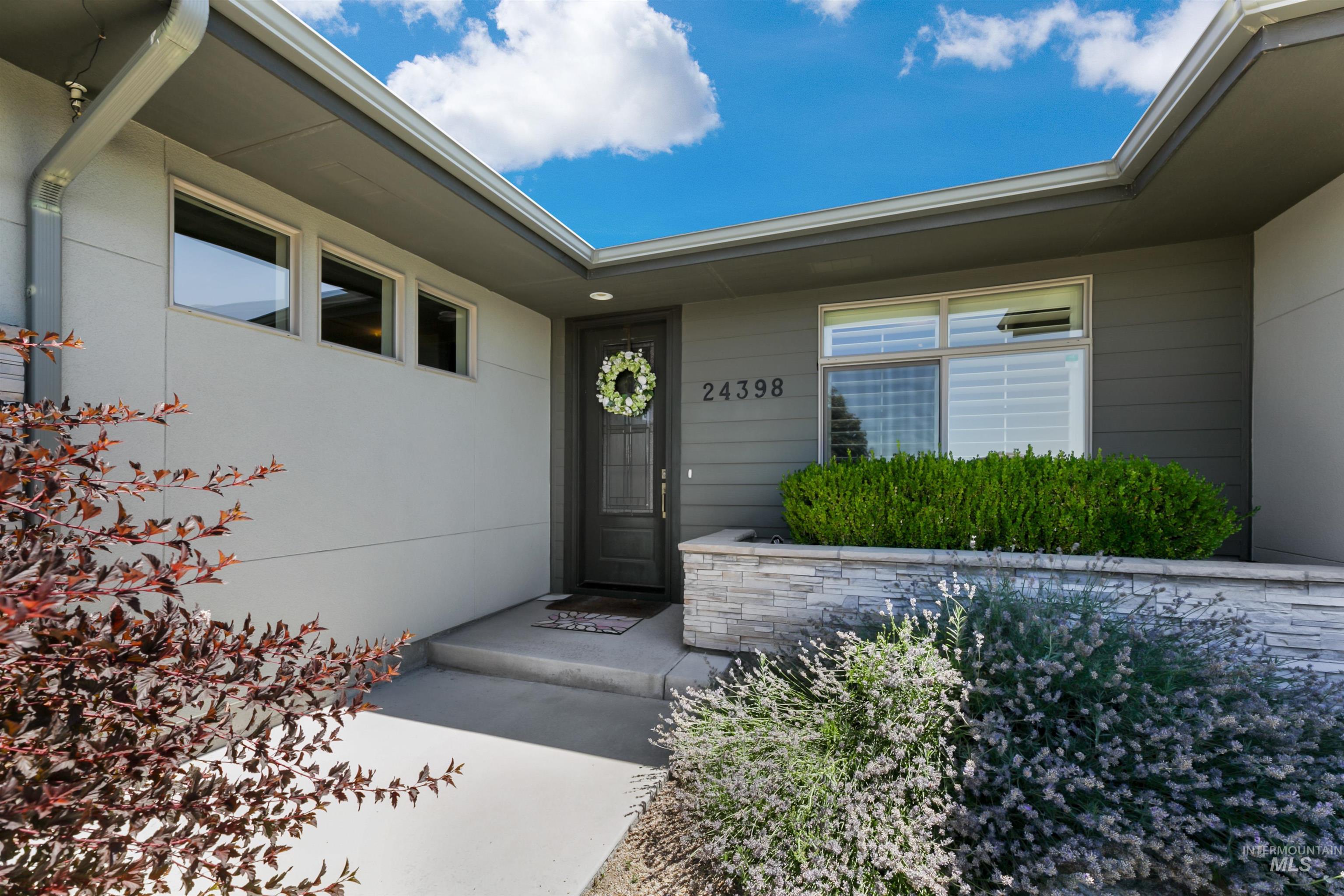24398 Tombstone Ridge Court Middleton, ID 83644 - Photo 2 of 47 Modern exterior featuring a dark gray entry door, light gray stucco, horizontal siding, and a stacked stone planter with shrubbery