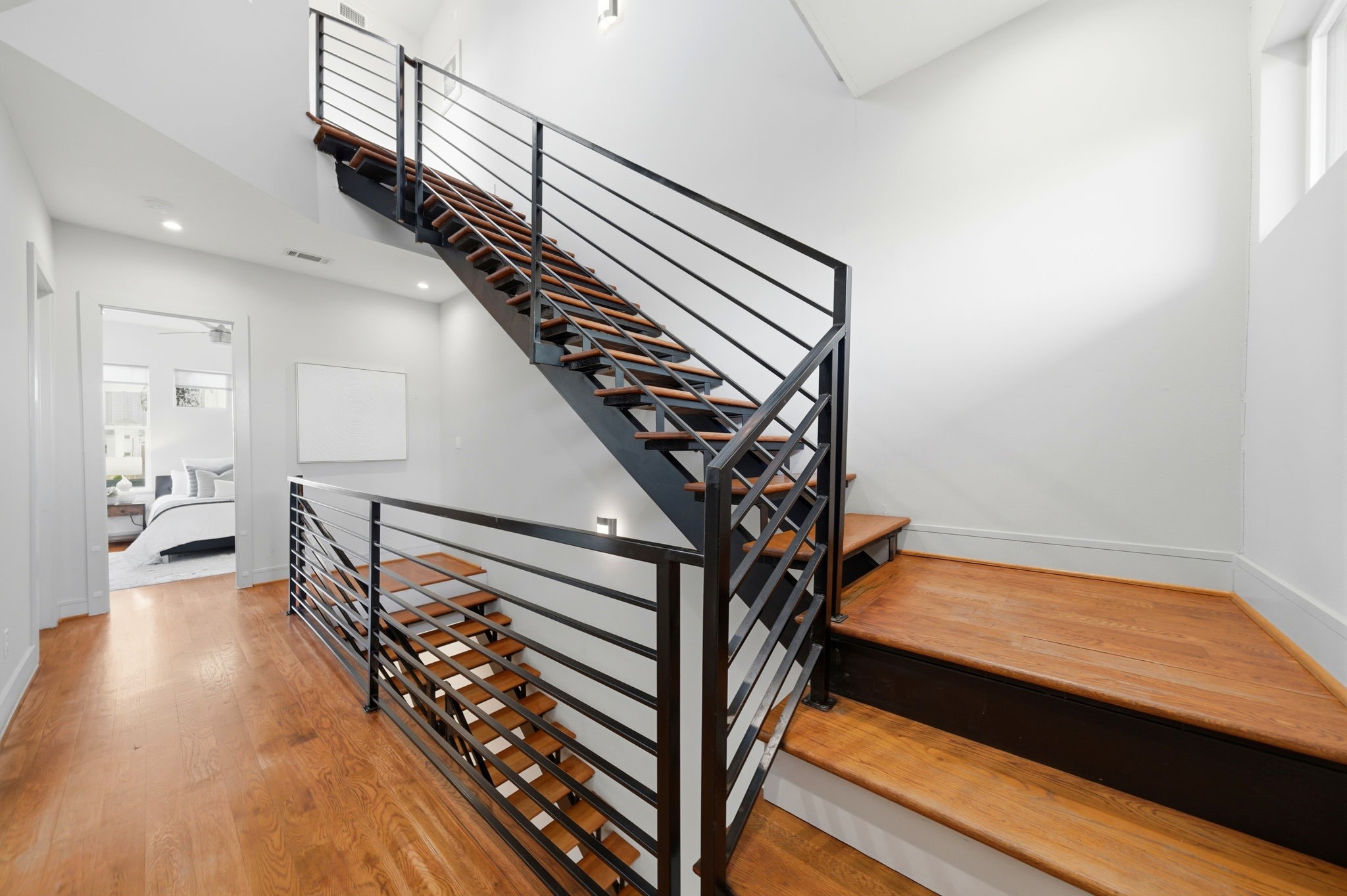 1405 Vermont Street, Unit A Houston, TX 77006 - Photo 36 of 46 Polished hardwood floors and a modern floating staircase with black steel railings define this expansive third-floor landing. Natural light streams from high windows, highlighting the designer finishes and accent lighting that guide the way toward the serene primary suite. This light-filled hallway showcases the home's contemporary architectural lines and seamless transitions between luxury living spaces.