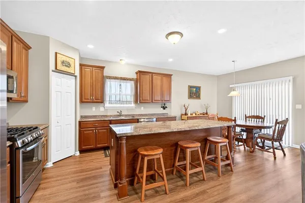 a kitchen with stainless steel appliances granite countertop a stove top oven a sink a dining table and chairs with wooden floor