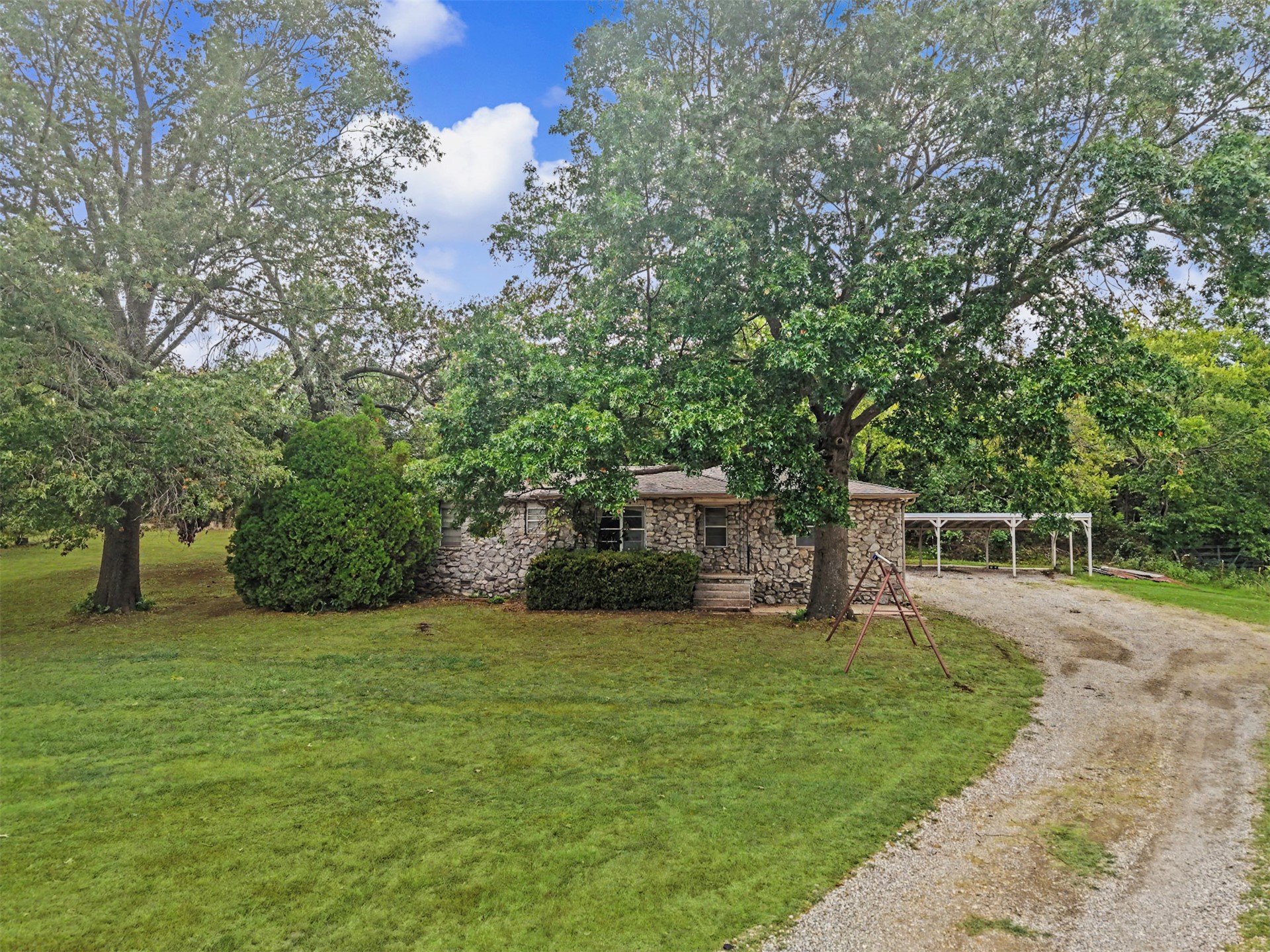 394290 West 4100th Road Skiatook, OK 74070 - Photo 5 of 41 Stone exterior home with a gravel driveway, mature trees, and an expansive lawn