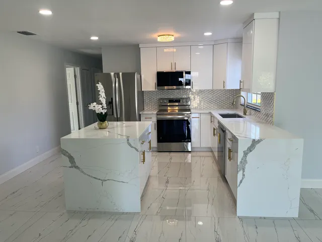 a large white kitchen with wooden floor and stainless steel appliances