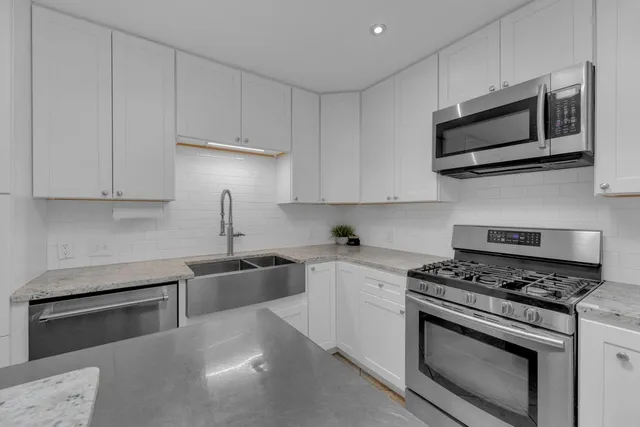 a kitchen with stainless steel appliances granite countertop grey cabinets a stove a microwave and a sink