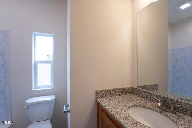 a bathroom with a granite countertop sink a toilet and a window