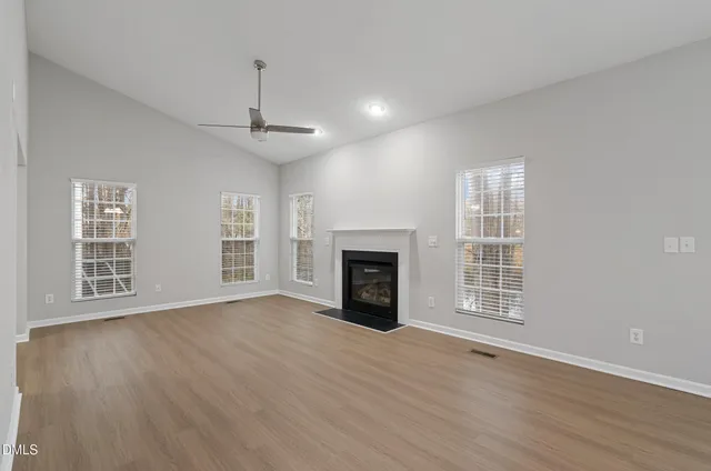 a view of an empty room with wooden floor fireplace and a window