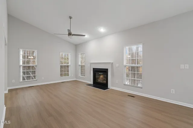 a view of an empty room with wooden floor fireplace and a window
