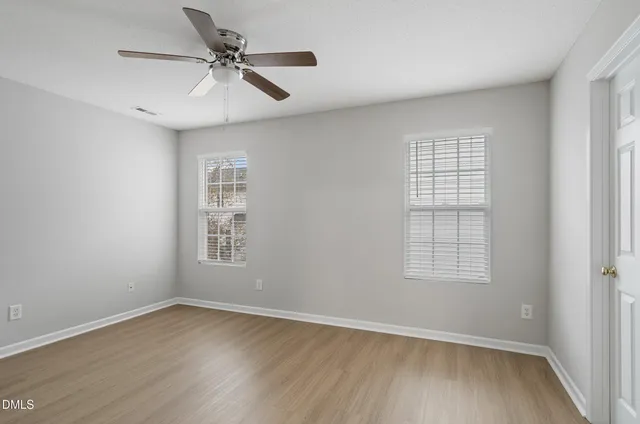 an empty room with wooden floor chandelier fan and windows