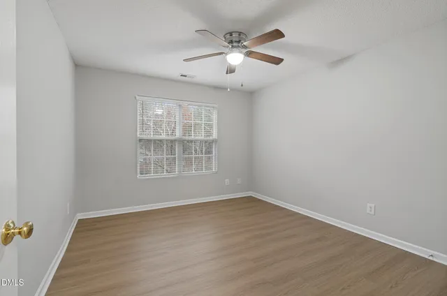 an empty room with wooden floor chandelier fan and windows
