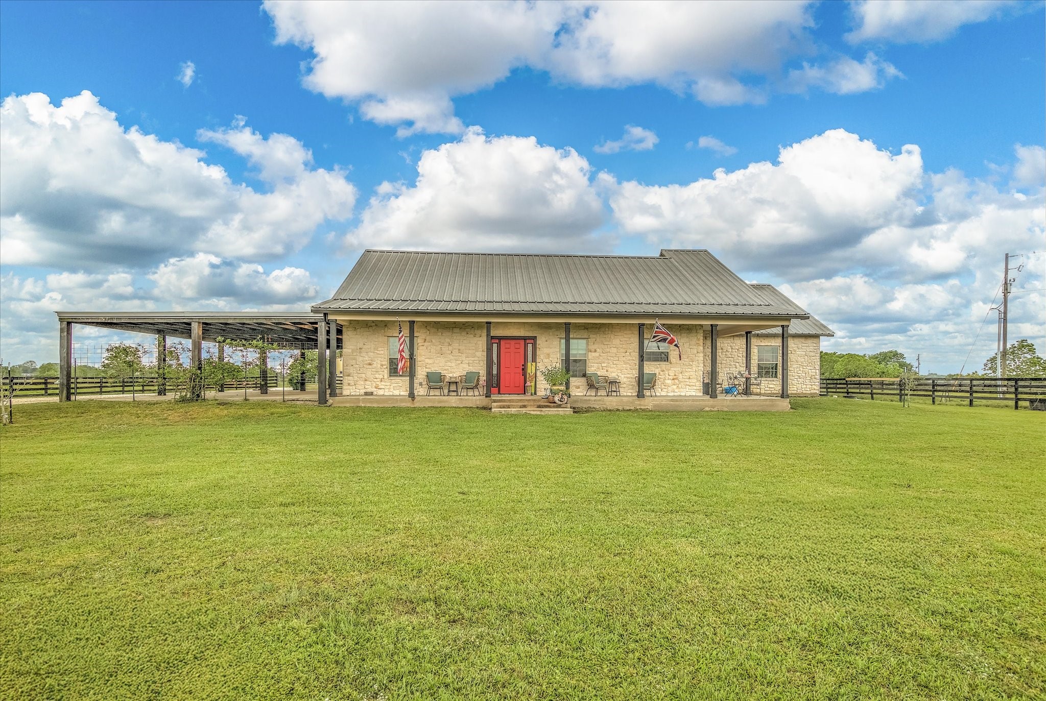 1755 McBride-Devillier Loop Winnie, TX 77665 - Photo 5 of 44 This charming home features a welcoming stone facade with a vibrant red door, set against a backdrop of expansive green lawns and open skies, offering a perfect blend of rustic elegance and serene country living.
