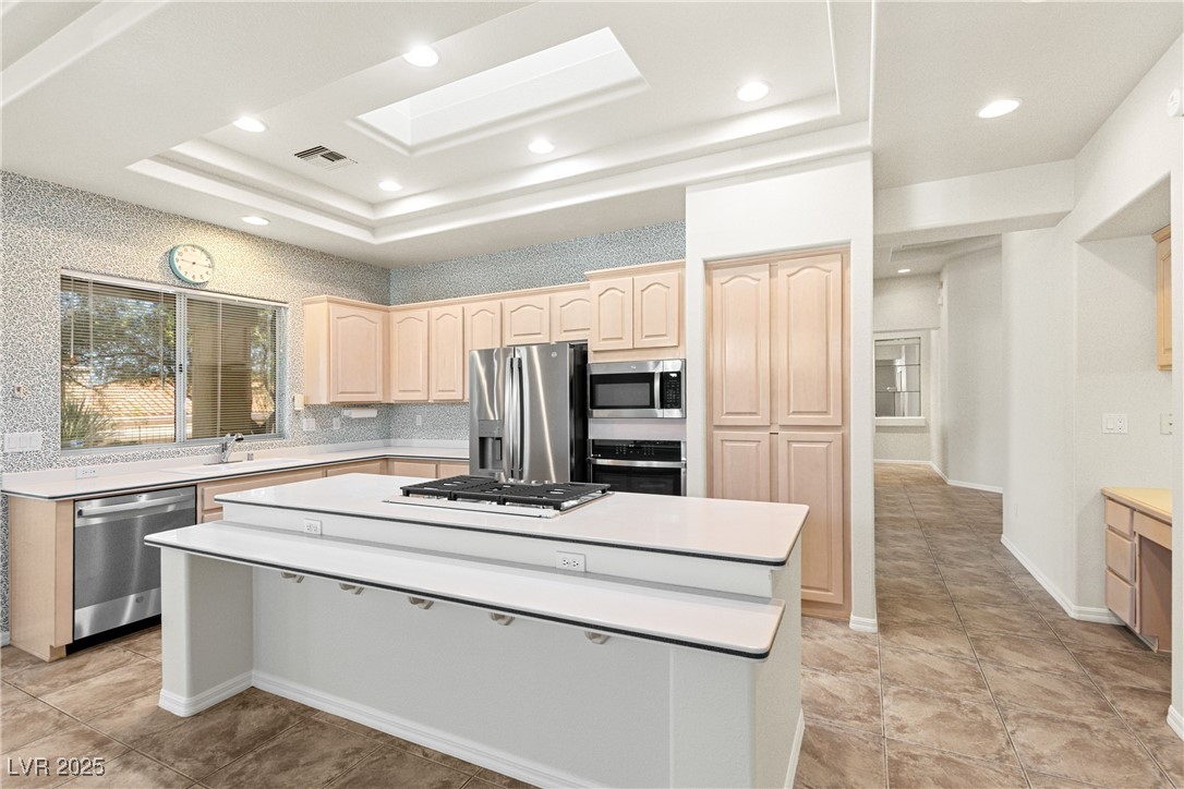 Kitchen featuring light countertops, light brown cabinetry, a tray ceiling, stainless steel appliances, and a skylight
