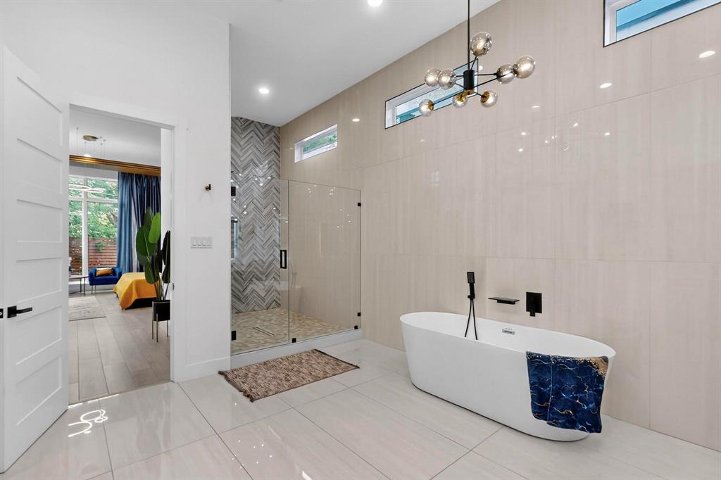 3946 North Cresthaven Road Dallas, TX 75209 - Photo 15 of 38 Contemporary bathroom featuring a freestanding soaking tub with floor-mounted black fixtures, a spacious glass-enclosed shower with chevron-patterned tile, and large format wall and floor tiling