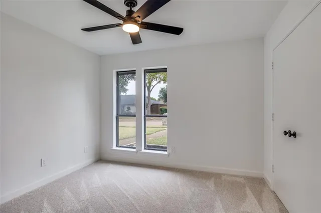 an empty room with chandelier fan and windows