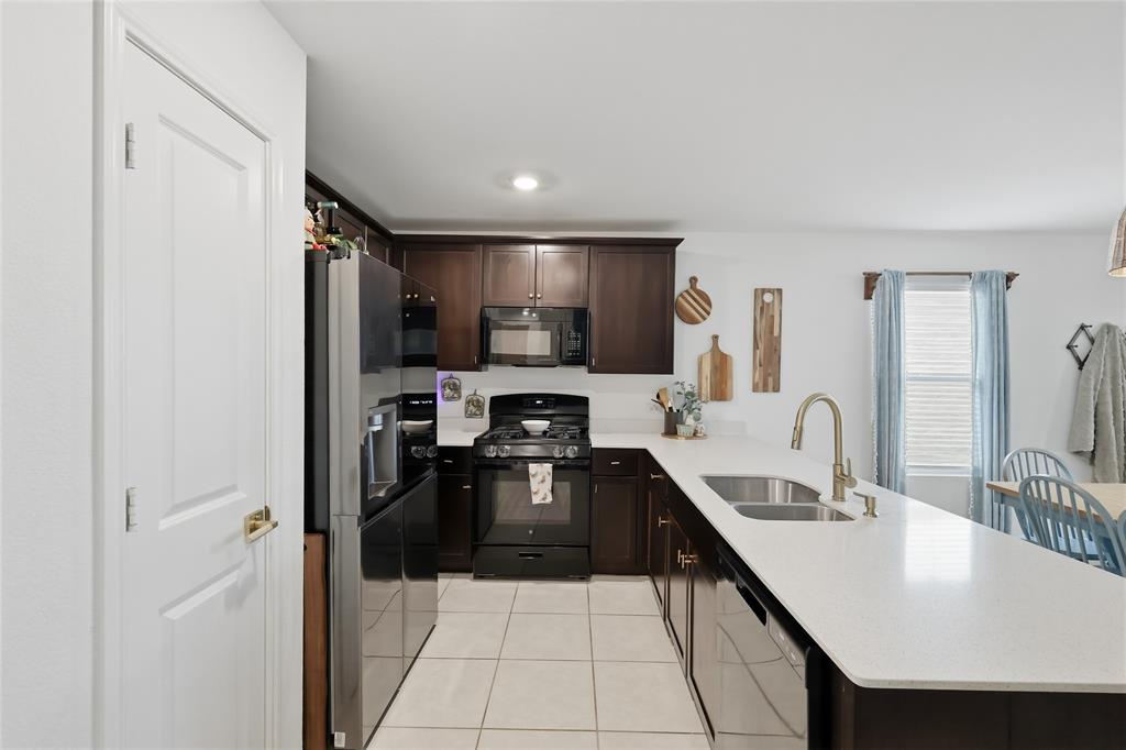312 Ranchito Pass Fort Worth, TX 76052 - Photo 13 of 30 Kitchen with dark wood finish cabinets, black appliances, a peninsula, light tile patterned floors, and light stone counters