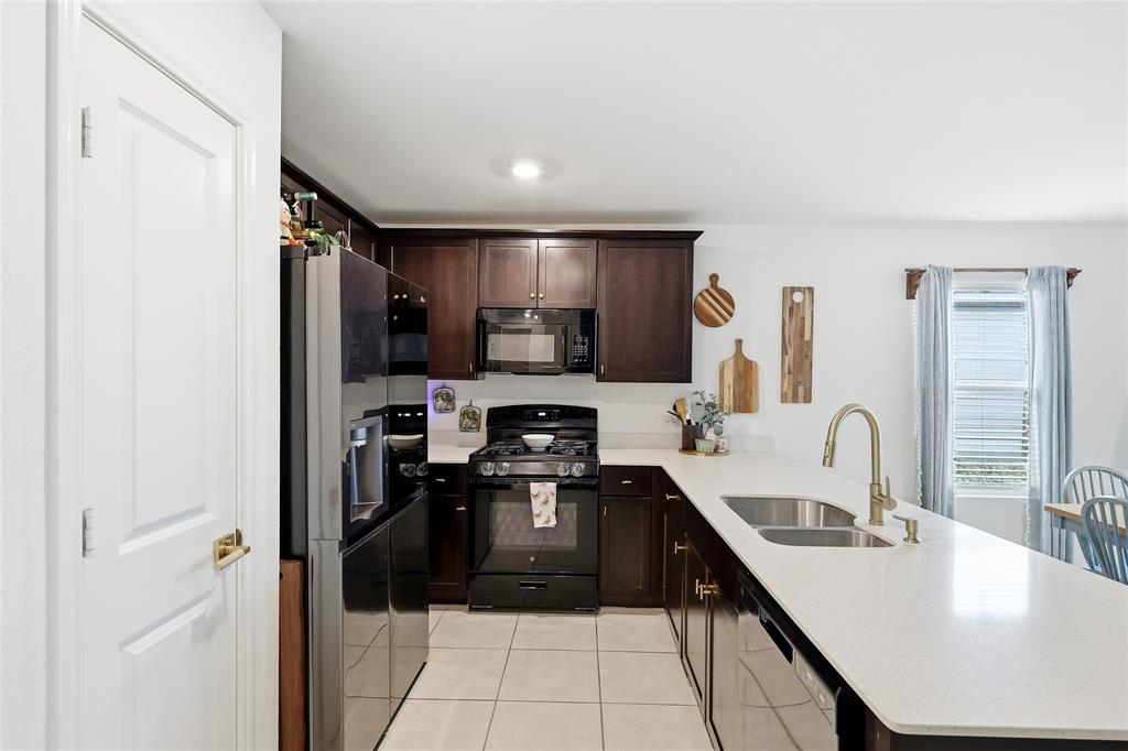 312 Ranchito Pass Fort Worth, TX 76052 - Photo 14 of 30 Kitchen with dark wood finish cabinetry, black appliances, a peninsula, light tile patterned floors, and light stone countertops