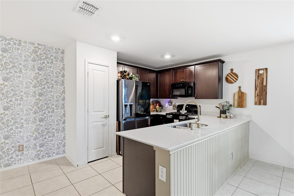 312 Ranchito Pass Fort Worth, TX 76052 - Photo 15 of 30 Kitchen with dark wood finish cabinets, stainless steel appliances, a peninsula, light tile patterned floors, and light stone counters