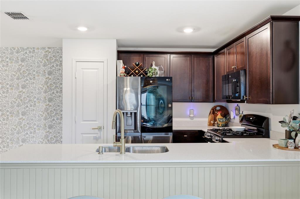 312 Ranchito Pass Fort Worth, TX 76052 - Photo 16 of 30 Kitchen with dark wood finish cabinets, a peninsula, wallpapered walls, black appliances, and light stone countertops