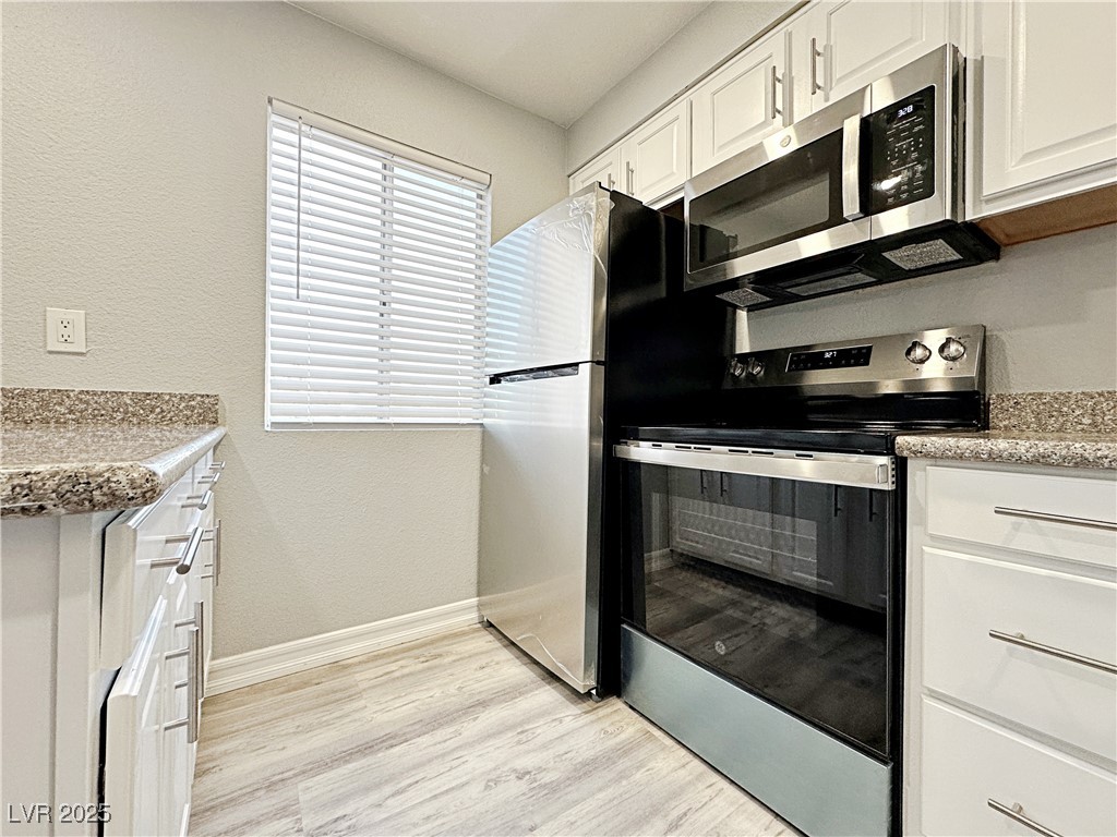 5080 Indian River Drive, Unit 400 Las Vegas, NV 89103 - Photo 11 of 29 Kitchen featuring appliances with stainless steel finishes, white cabinets, light wood-type flooring, a textured wall, and light stone countertops