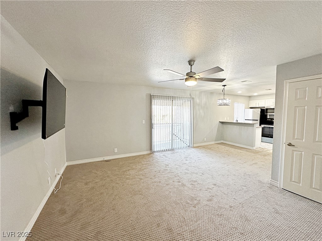 5080 Indian River Drive, Unit 400 Las Vegas, NV 89103 - Photo 5 of 29 Unfurnished living room with light carpet, a textured ceiling, and a ceiling fan