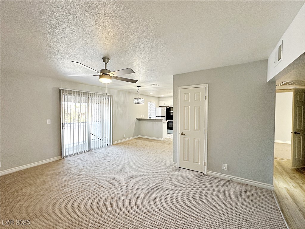 5080 Indian River Drive, Unit 400 Las Vegas, NV 89103 - Photo 6 of 29 Unfurnished living room featuring a textured ceiling, light colored carpet, a ceiling fan, and a textured wall