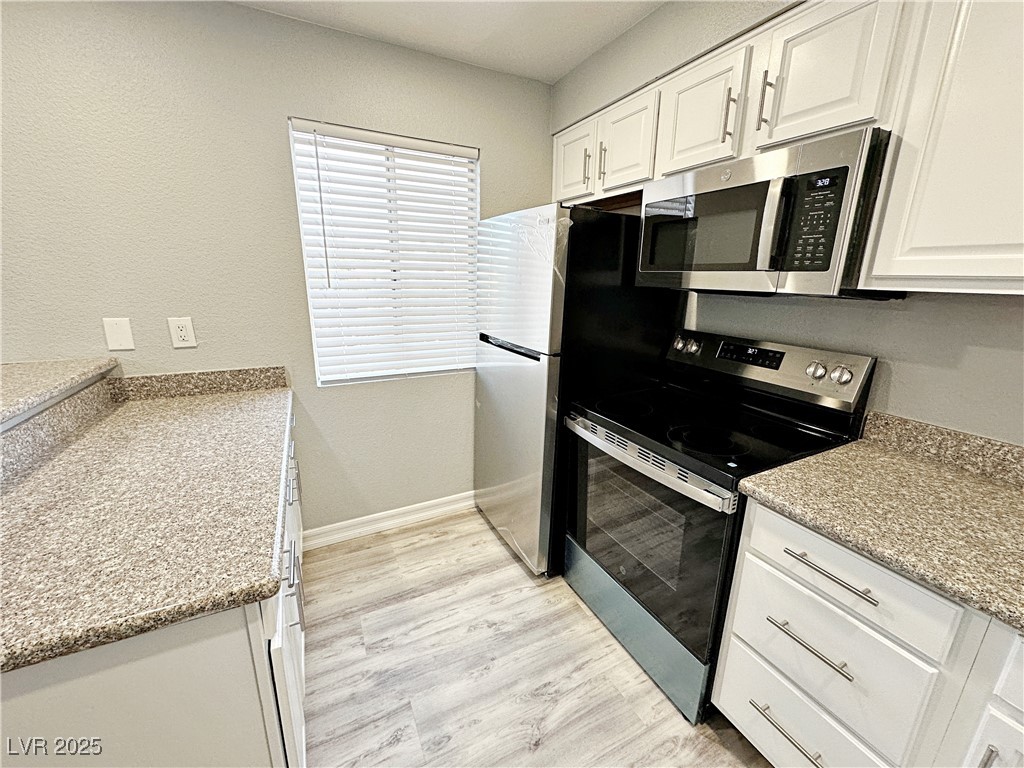 5080 Indian River Drive, Unit 400 Las Vegas, NV 89103 - Photo 9 of 29 Kitchen with stainless steel appliances, white cabinets, light wood-style floors, and light stone counters