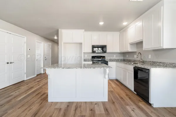 a large kitchen with kitchen island granite countertop a stove a sink a refrigerator and white cabinets with wooden floor