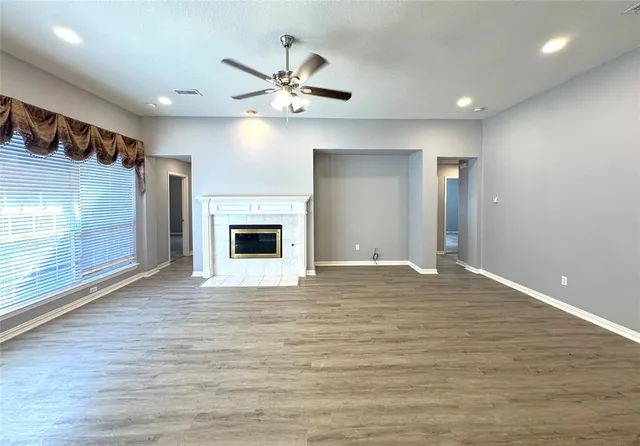 a view of an empty room with wooden floor fireplace and a window