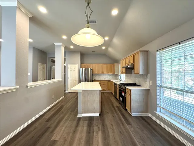 a large kitchen with stainless steel appliances granite countertop a stove oven and a large window with wooden floors