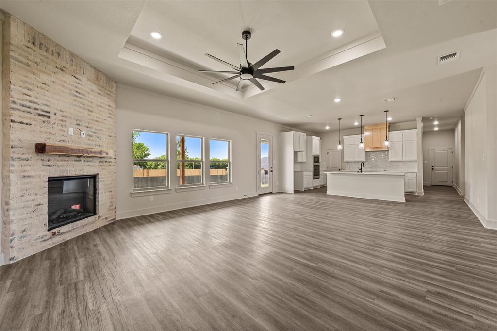 138 Dana Pt Road Lorena, TX 76655 - Photo 7 of 24 Expansive interior featuring wood-finish flooring, a tray ceiling with a contemporary fan, and a painted brick fireplace with a wood mantel