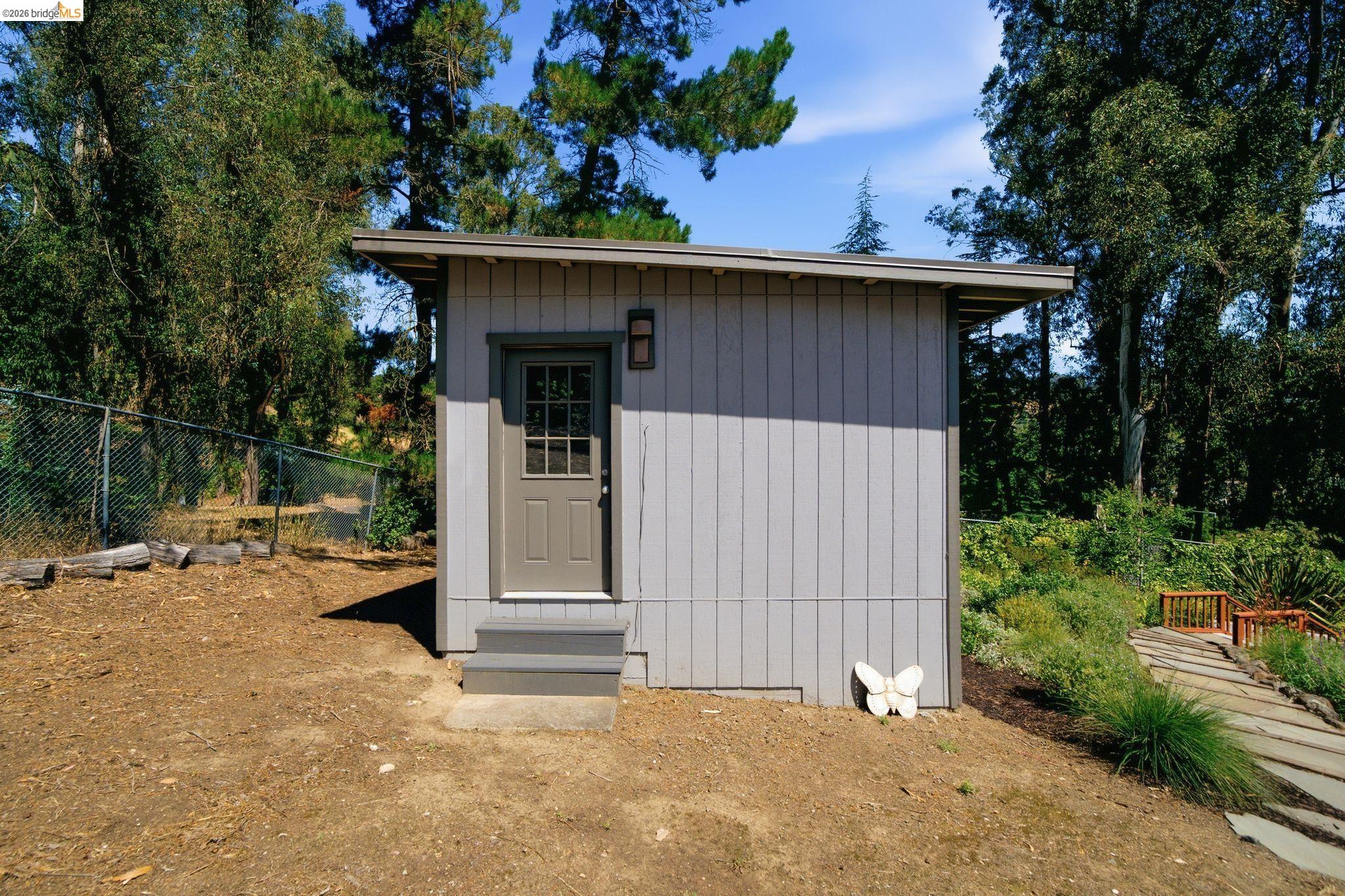 11133 Golf Links Road Oakland, CA 94605 - Photo 49 of 57 Freestanding structure featuring board and batten siding, a single entry door with window panes, and a small exterior light fixture