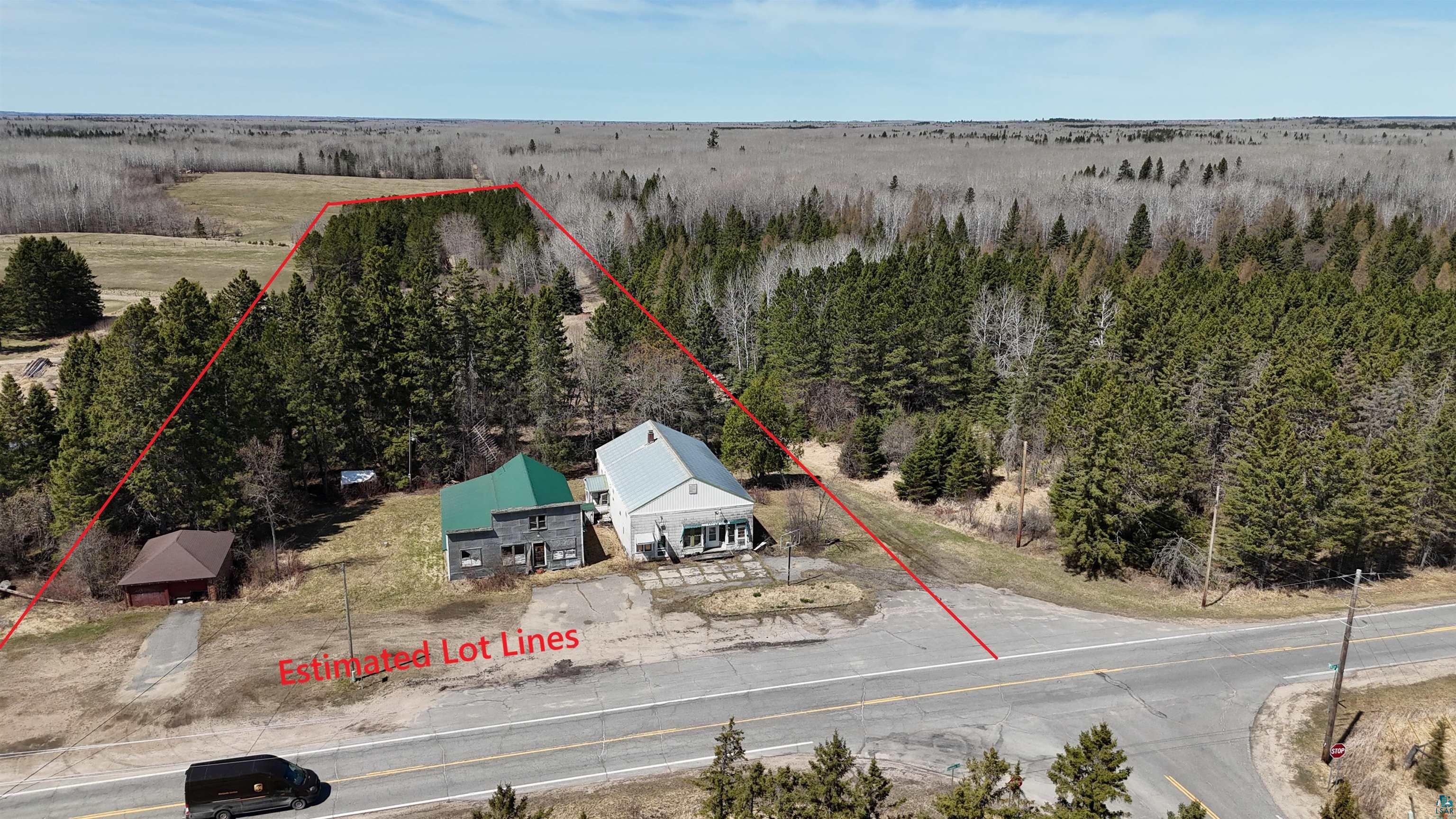 3293 South Greaney Road Orr, MN 55771 - Photo 15 of 17 Property featuring two structures, a gray-sided building with a light-colored roof and a green-roofed building, surrounded by dense evergreen trees